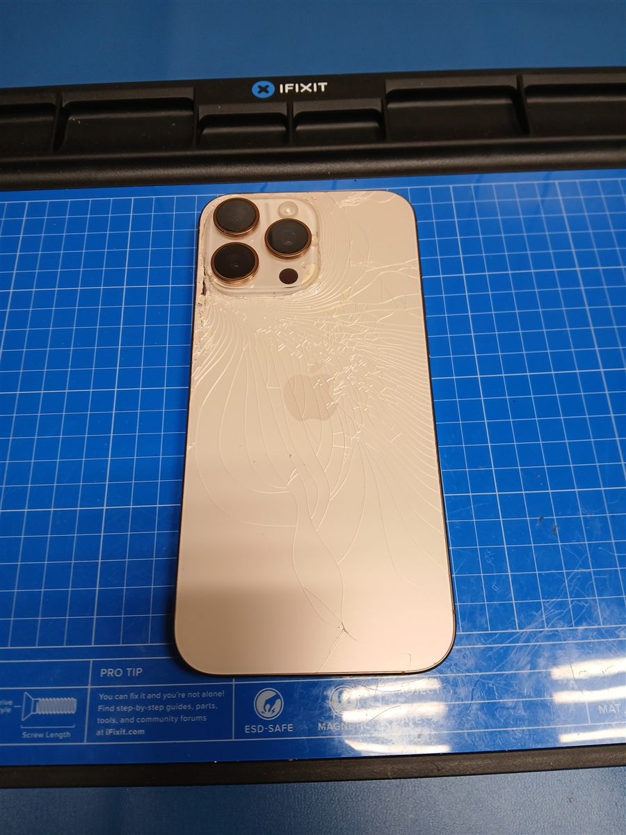 iPhone 16 Pro Max face down on the bench mat before repair: back glass shattered in a web radiating from the camera housing